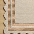 Top-down angled view of Scottie Ivory Rust Rug on wood floor highlighting scalloped edges and striped border