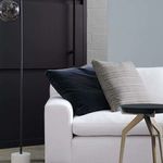 Close-up side view showing armrest and two pillows against modern interior with dark wall and floor lamp