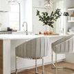 Two stools styled in a bright kitchen with wood flooring and white counters enhancing the polished nickel base.
