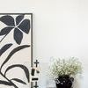 painting leaning against wall on wooden surface next to black vase filled with white flowers and small decorative objects
