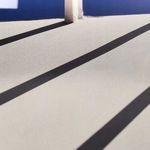 Close-up of diagonal shadows cast by vertical beams across light gray surface in the photograph