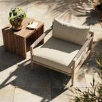 Chair styled outdoors on stone tile patio with wooden side table and potted plant