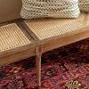 Close-up of bench seat caning texture with patterned pillows and colorful rug beneath