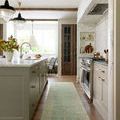 Long runner style rug in kitchen with green cabinetry and wooden floor beneath
