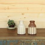 Two Avi Vases side by side on wooden table, one in classic white and one in brown with white ribbed pattern