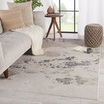 Styled room view with the rug under sofa and table, accented by a knitted pouf and neutral cushions.