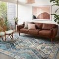 Zion Ocean Gold Rug styled in living room under brown leather sofa with wicker chair and natural light from window