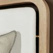 Close-up of rounded corner of oak frame and white leather upholstered headboard