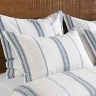 Set of three shams styled on bed with wooden headboard, showcasing texture and scale of stripes