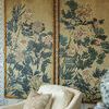 Framed botanical paintings viewed from side with off-white armchair and wooden side table holding blue and white ceramics