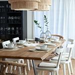 Dining table styled with the oval platter among white chairs and wicker seating in a bright room with sheer curtains
