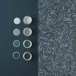 Salix Leaves Wallpaper sample displayed next to matching green and blue paint cans on dark wall