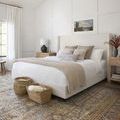 Layla rug partially under a white bed in a bright bedroom with woven baskets on light wooden floor