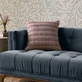 Poe Burgundy Pillow styled on a navy velvet tufted sofa against patterned wallpaper