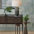 Room setting including bronze Castor Accent Table beside dark wood console with white lamp, framed wall art behind