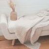 Throw draped over bench in living room with wooden floor and woven vase beside it