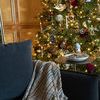 Plaid throw casually draped over dark chair arm in cozy room with decorated Christmas tree in background