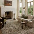 Rug styled in living room with cream sofa, green armchair, and large arched windows showing scale and color