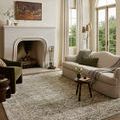 Olive and ivory rug styled in a living room with a white sofa, green chair, and fireplace