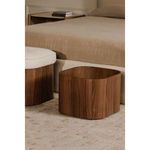 Sonny Stool storage base beside bed, highlighting rounded walnut veneer and beige linens