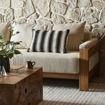 Ditmar outdoor pillow styled on cream couch with wood armrest and stone wall background