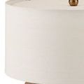 Close-up of beige drum shade’s top edge with visible brass finial detail above textured concrete base