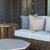 QS Audrey Coffee Table placed on woven outdoor rug next to wicker sofa with pillows on covered patio