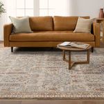 Rug under modern caramel leather sofa and round wooden coffee table with open book on top