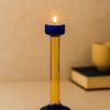 Yellow and blue glass candle holder with lit flame on a table next to books and cup