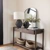 Mirror hung on wall above dark wood console table styled with lamp, plant, books, and woven baskets underneath