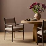 Dining chair shown angled near round wooden dining table with flowers and tableware in brown room setting