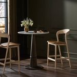 Two Amare Stools styled around round pedestal table in dark room with window and flower vase