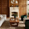 Heritage Bark rug styled in a living room with wood panel walls, fireplace, green accent chairs, and a wooden coffee table
