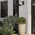 Outdoor installed Mariner Wall Sconce with light on, casting shadow on white brick facade