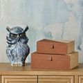Two stacked leather and raffia boxes styled with ceramic owl sculpture on wood furniture