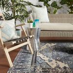 Side view of the rug near a black strap wood chair and metal side table in an outdoor porch setting.