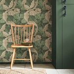William Morris Acanthus Wallpaper installed on wall behind light wood chair with books and cup, next to green painted door