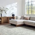Charcoal rug placed in a bright living room under a beige sectional sofa near large black grid window