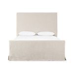 Angled front view of queen bed with full slipcover skirt touching floor and pillows arranged on mattress
