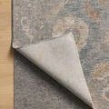 Corner of rug lifted to reveal its light-colored backing and thickness against a wooden floor
