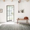 Bellamy Lagoon Rug in open living space with natural light, wood bench, leather bag, and beige shoes