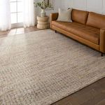 Living room context with rug laid out, a caramel leather sofa, cream pillow, light hardwood floor, and white wall