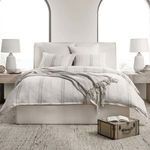 Front-facing wide shot of bed with striped duvet, pillows, and throw in minimalist room with arched windows