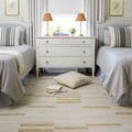 Max rug shown in a bedroom setting between two beds with gray linens and striped pillows