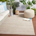 Light taupe rug styled in an outdoor patio setting with wicker sofa, plants, pouf, and wooden deck flooring