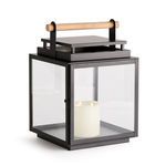 Square outdoor lantern with wide glass panes, black metal frame, and a teak wood handle, containing a lit candle