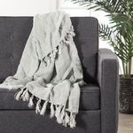 Gray linen throw draped casually over dark gray upholstered armchair with plant in background