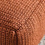 Detailed close-up of the woven stitching and textured yarn on the surface of the rust-colored pouf