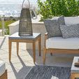 Chesapeake End Table styled outdoors by ocean with wicker lantern on top, next to white cushioned seating