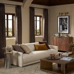 Brass double sconce installed in a living room with neutral sofa, wood furniture, and framed art